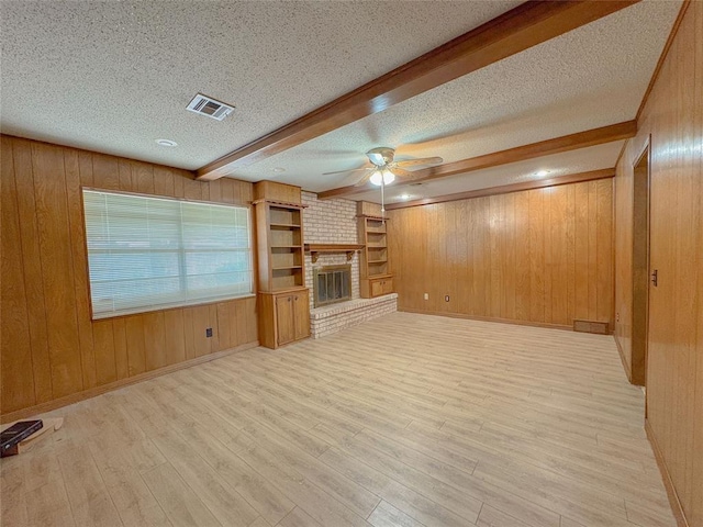 2313 SW 91st St, Oklahoma City, OK 73159 - unfurnished living room featuring a ceiling fan, wood walls, light wood-style flooring, a brick fireplace, and beamed ceiling
