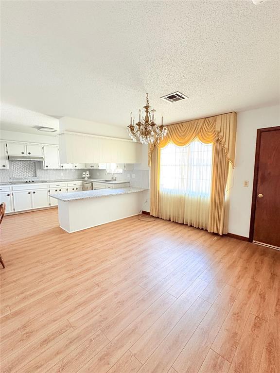 2313 SW 91st St, Oklahoma City, OK 73159 - kitchen featuring a chandelier, a peninsula, a textured ceiling, light countertops, and white cabinetry