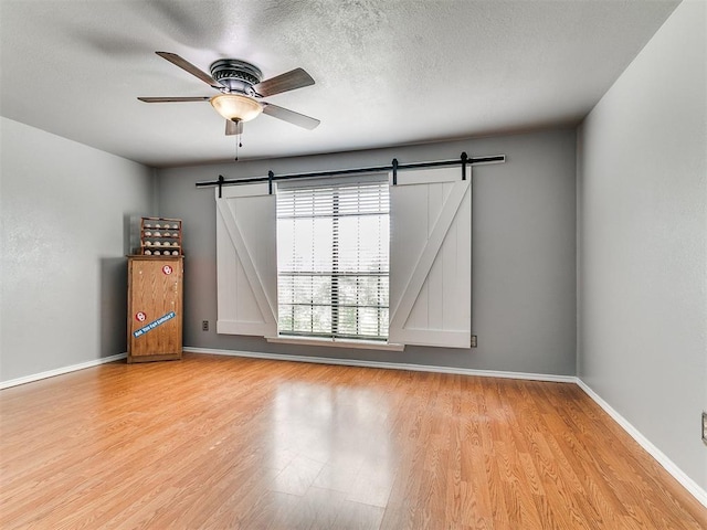 13005 Willowcrest Ln, Oklahoma City, OK 73170 - spare room featuring a barn door, light wood finished floors, a ceiling fan, and a textured ceiling