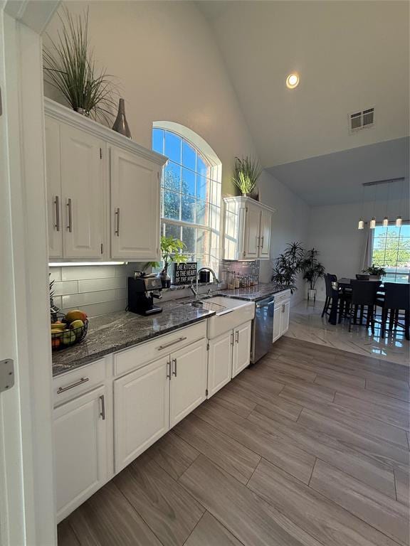 1030 Belmonte Ct, Yukon, OK 73099 - kitchen featuring stainless steel dishwasher, high vaulted ceiling, white cabinets, recessed lighting, and dark stone counters