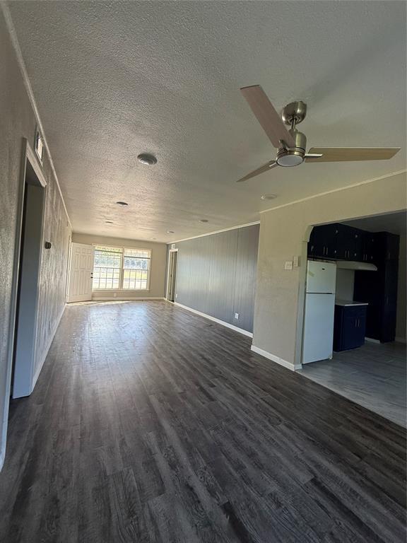 3208 N Roff Ave, Oklahoma City, OK 73112 - unfurnished living room with dark wood-style flooring, a textured ceiling, a ceiling fan, and baseboards