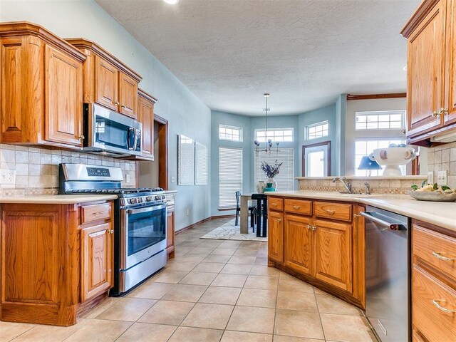 2508 Hamden Ave, Norman, OK 73069 - kitchen featuring appliances with stainless steel finishes, brown cabinetry, light tile patterned flooring, light countertops, and tasteful backsplash