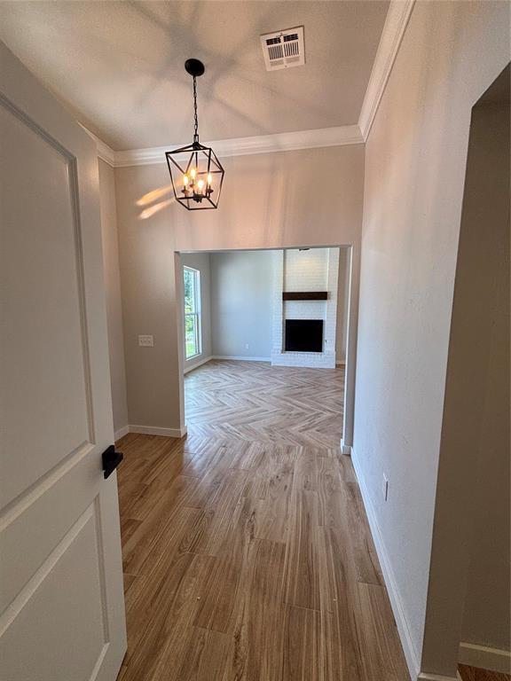 10501 Reiter Dr, Midwest City, OK 73130 - spare room featuring crown molding, baseboards, a chandelier, wood finished floors, and a fireplace