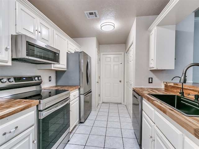 105 Taos, Edmond, OK 73013 - kitchen with stainless steel appliances, wooden counters, white cabinets, a textured ceiling, and light tile patterned floors