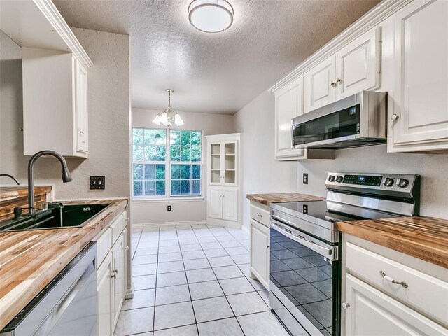 105 Taos, Edmond, OK 73013 - kitchen featuring appliances with stainless steel finishes, butcher block countertops, a textured ceiling, a chandelier, and white cabinetry