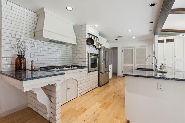 2241 NW 56th St, Oklahoma City, OK 73112 - kitchen with stainless steel appliances, custom exhaust hood, a sink, light wood-type flooring, and decorative backsplash