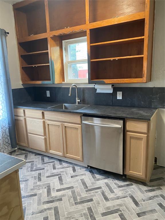 640 SE 20th St, Oklahoma City, OK 73129 - kitchen featuring stainless steel dishwasher, open shelves, a sink, dark countertops, and brick patterned floors