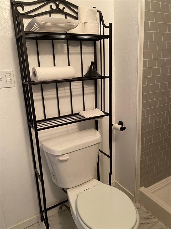 640 SE 20th St, Oklahoma City, OK 73129 - bathroom with a shower stall, toilet, a textured wall, and baseboards