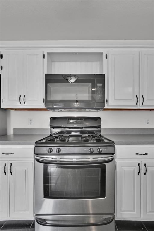 1101 Wendy Ln, Altus, OK 73521 - kitchen featuring stainless steel range with gas cooktop, black microwave, and white cabinetry
