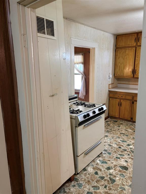 316 N Crenshaw St, Wayne, OK 73080 - kitchen featuring white gas range oven, brown cabinets, stone finish flooring, light countertops, and wooden walls