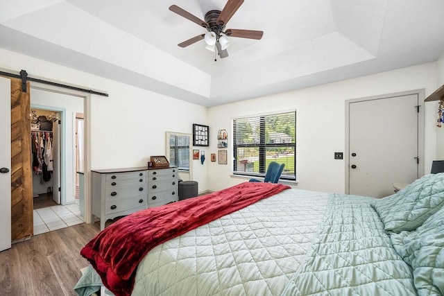 11110 Jeffords Ave, Choctaw, OK 73020 - bedroom with wood finished floors, a barn door, a tray ceiling, and a ceiling fan