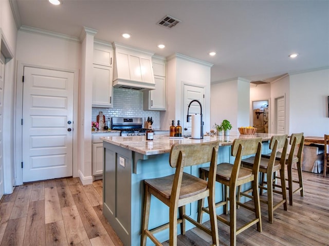 11611 Carefree Ln, Shawnee, OK 74804 - kitchen with stainless steel gas range, ornamental molding, premium range hood, light wood-type flooring, and an island with sink