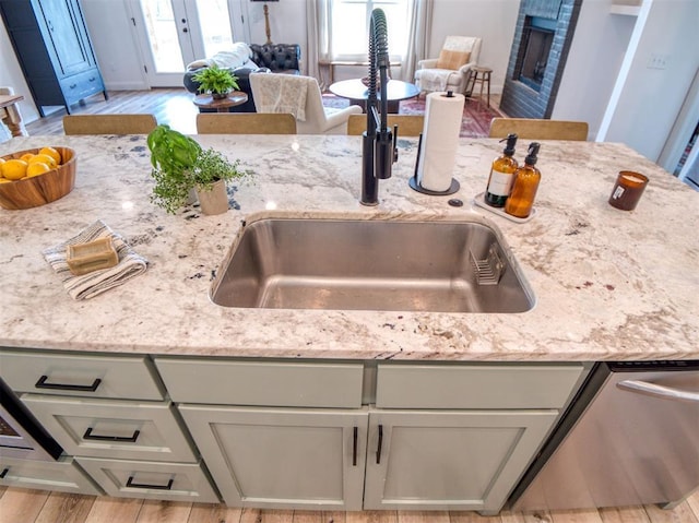 11611 Carefree Ln, Shawnee, OK 74804 - kitchen view of a sink, light stone counters, dishwasher, a brick fireplace, and wood finished floors