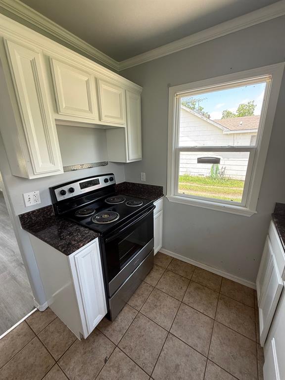 1707 N Louisa Ave, Shawnee, OK 74804 - kitchen with stainless steel range with electric cooktop, ornamental molding, light tile patterned floors, baseboards, and white cabinets