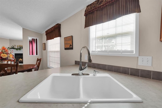 1318 N Cook St, Cordell, OK 73632 - kitchen featuring a sink, healthy amount of natural light, a textured ceiling, lofted ceiling, and a warm lit fireplace