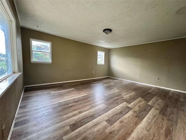 1502 S 12th St, Chickasha, OK 73018 - unfurnished room with a textured ceiling, wood finished floors, plenty of natural light, a textured wall, and baseboards