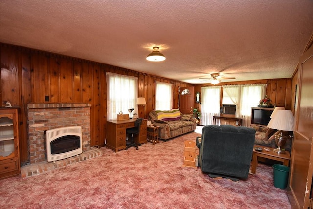 220 E Tiger Ave, Wetumka, OK 74883 - carpeted living area featuring heating unit, a textured ceiling, wooden walls, a fireplace, and a ceiling fan