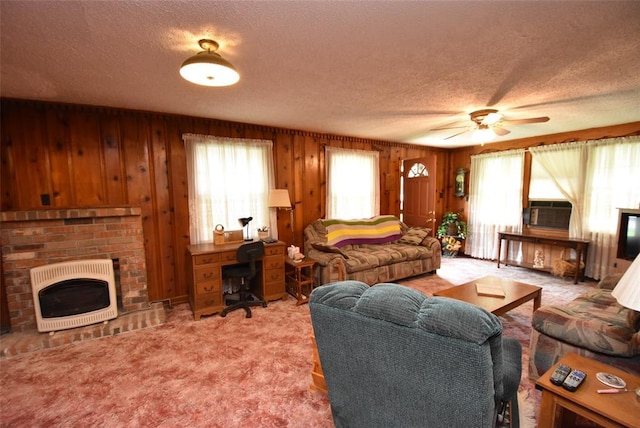 220 E Tiger Ave, Wetumka, OK 74883 - carpeted living room with heating unit, a textured ceiling, a fireplace, wood walls, and a ceiling fan