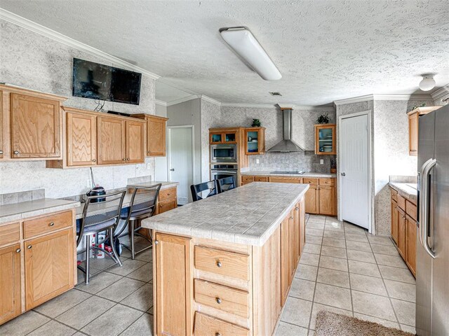 19108 Finn Ridge Rd, Purcell, OK 73080 - kitchen featuring wall chimney exhaust hood, appliances with stainless steel finishes, light tile patterned floors, a center island, and ornamental molding