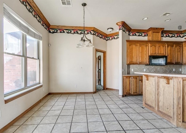 5704 Bent Creek Dr, Oklahoma City, OK 73135 - kitchen with black microwave, tasteful backsplash, light countertops, brown cabinets, and hanging light fixtures