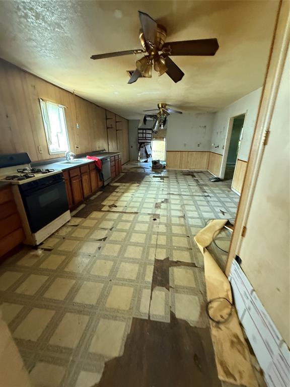 1321 SW 13th St, Oklahoma City, OK 73108 - kitchen featuring gas range, wood walls, brown cabinets, ceiling fan, and a sink