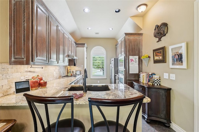 3201 Pinehurst Dr, Norman, OK 73072 - kitchen with a peninsula, a breakfast bar, decorative backsplash, light stone counters, and vaulted ceiling