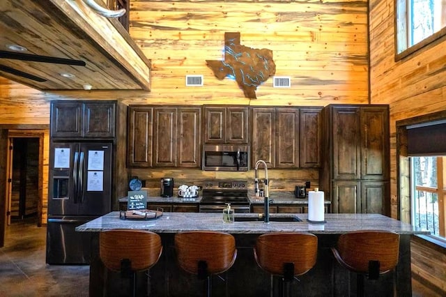 161 Champion Way, Broken Bow, OK 74728 - kitchen with stainless steel appliances, wooden walls, a sink, a breakfast bar area, and a kitchen island with sink