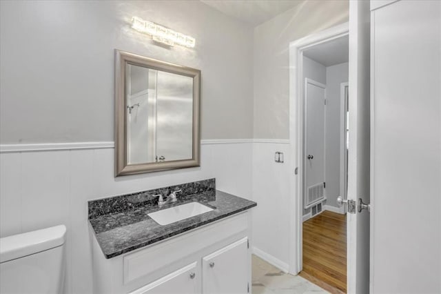 5712 N Roff Ave, Oklahoma City, OK 73112 - bathroom featuring vanity, toilet, wainscoting, and marble look tiles
