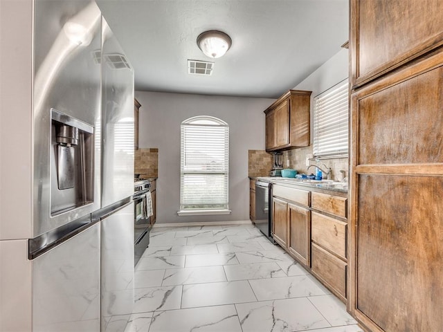 5805 Marblewood Dr, Oklahoma City, OK 73179 - kitchen with stainless steel appliances, light marble finish floors, brown cabinets, and decorative backsplash