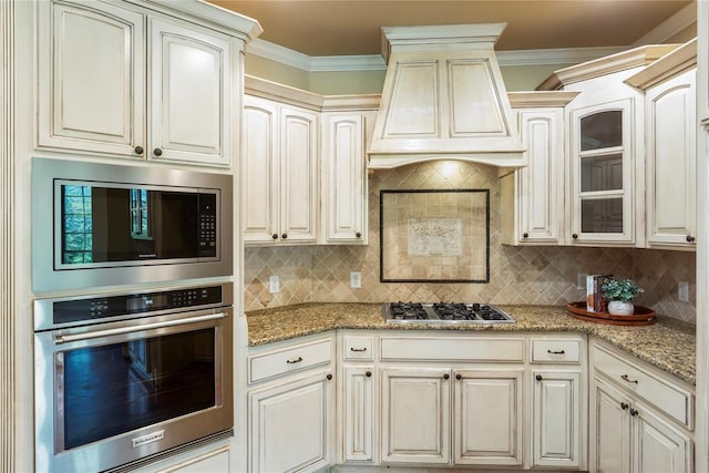 6373 Stone Valley Dr, Edmond, OK 73034 - kitchen featuring stainless steel appliances, decorative backsplash, light stone counters, glass insert cabinets, and crown molding