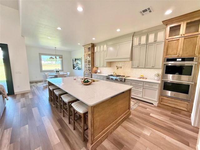 3320 Somerset Farms Rd, Newalla, OK 74857 - kitchen featuring stainless steel appliances, a sink, light wood-style floors, a kitchen island with sink, and decorative backsplash