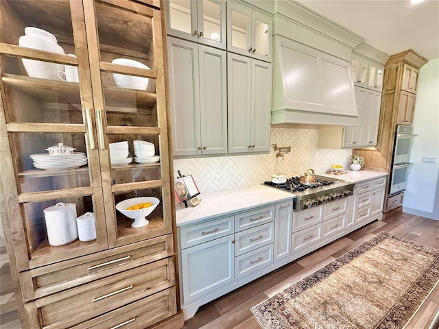 3320 Somerset Farms Rd, Newalla, OK 74857 - kitchen with appliances with stainless steel finishes, backsplash, glass insert cabinets, dark wood-style flooring, and custom range hood