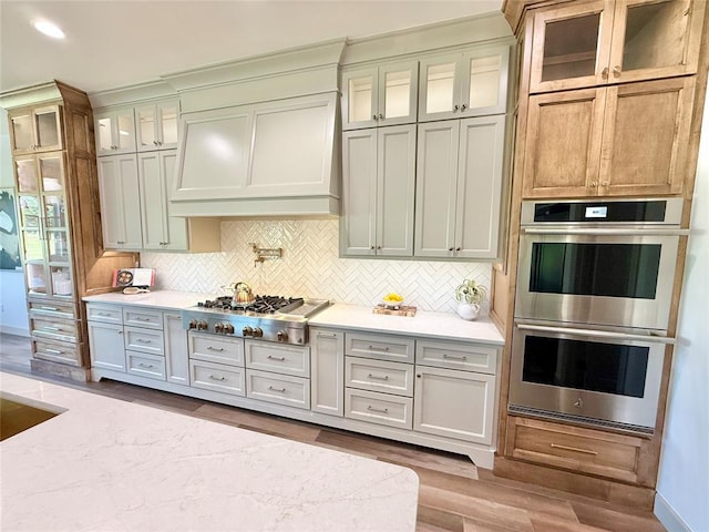 3320 Somerset Farms Rd, Newalla, OK 74857 - kitchen with stainless steel appliances, custom range hood, backsplash, wood finished floors, and glass insert cabinets