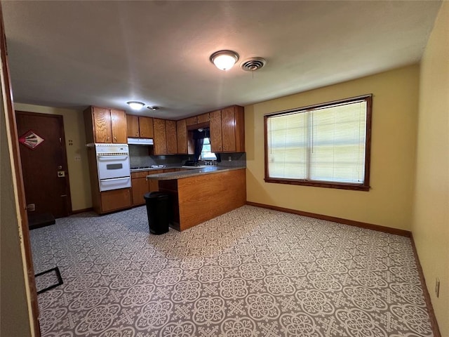 811 N Broadway St, Broken Bow, OK 74728 - kitchen featuring a warming drawer, oven, brown cabinets, a peninsula, and baseboards