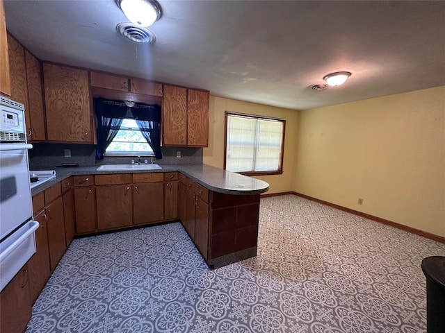 811 N Broadway St, Broken Bow, OK 74728 - kitchen featuring dark countertops, a sink, a peninsula, and brown cabinetry