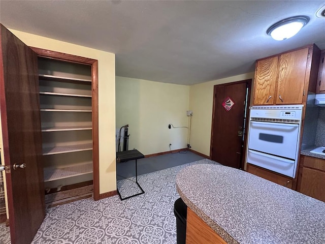 811 N Broadway St, Broken Bow, OK 74728 - kitchen featuring white oven, a warming drawer, brown cabinetry, and baseboards