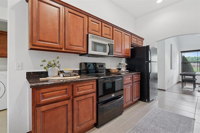 709 S Greengate Dr, Yukon, OK 73099 - kitchen with black appliances, washer / dryer, light tile patterned floors, dark stone counters, and brown cabinetry