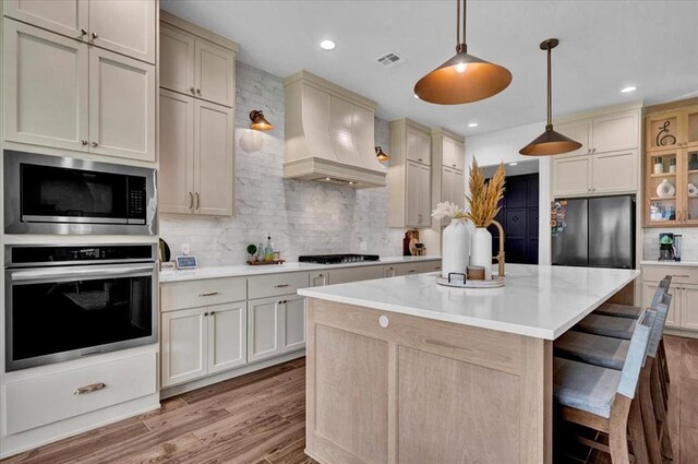1049 Dorsi Way, Newcastle, OK 73065 - kitchen featuring appliances with stainless steel finishes, custom exhaust hood, light countertops, decorative backsplash, and light wood-style flooring