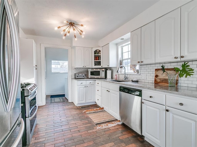 2647 NW 24th St, Oklahoma City, OK 73107 - kitchen with appliances with stainless steel finishes, a sink, brick floors, decorative backsplash, and white cabinets