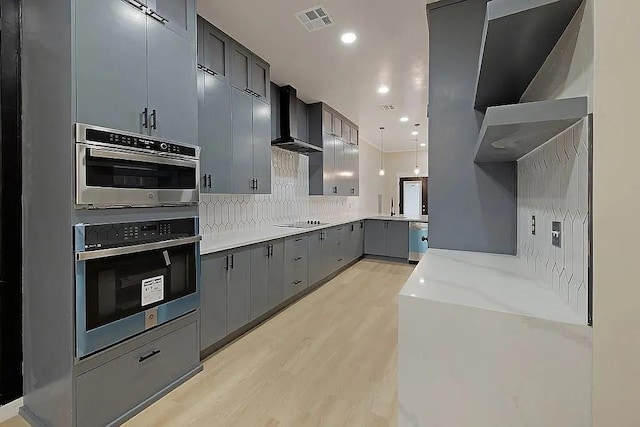 1533 NE 26th St, Oklahoma City, OK 73111 - kitchen featuring wall chimney range hood, light wood finished floors, gray cabinets, decorative backsplash, and appliances with stainless steel finishes