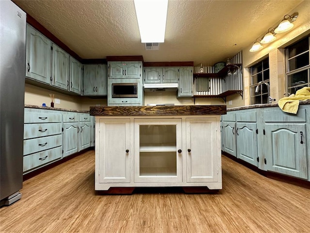20973 US Highway 62, Altus, OK 73521 - kitchen featuring a textured ceiling, stainless steel appliances, open shelves, wood finished floors, and dark countertops