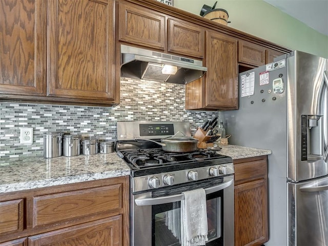 1816 Concord Pl, Norman, OK 73071 - kitchen with stainless steel appliances, under cabinet range hood, decorative backsplash, brown cabinets, and light stone countertops