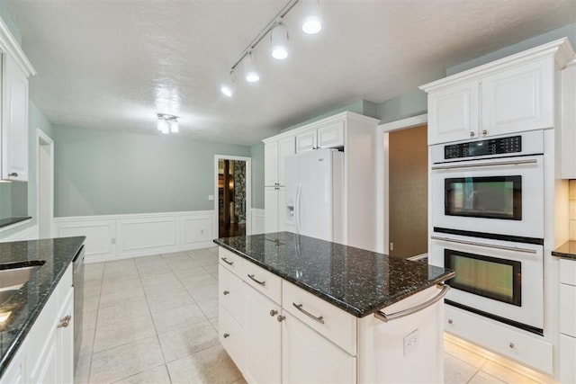4208 Briarcrest St, Norman, OK 73072 - kitchen featuring white appliances, white cabinetry, wainscoting, a center island, and dark stone countertops