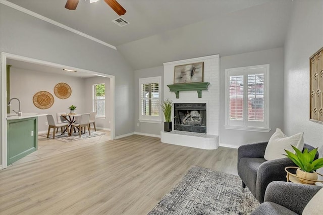 2309 NW 157th Ter, Edmond, OK 73013 - living room featuring vaulted ceiling, light wood-style flooring, a brick fireplace, ceiling fan, and baseboards