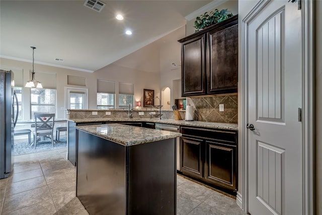 2717 Cordgrass Ln, Edmond, OK 73013 - kitchen featuring appliances with stainless steel finishes, tasteful backsplash, dark brown cabinets, light stone countertops, and a center island