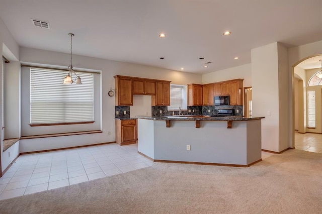 832 Elm Creek Dr, Moore, OK 73160 - kitchen with black microwave, arched walkways, brown cabinetry, a breakfast bar area, and tasteful backsplash