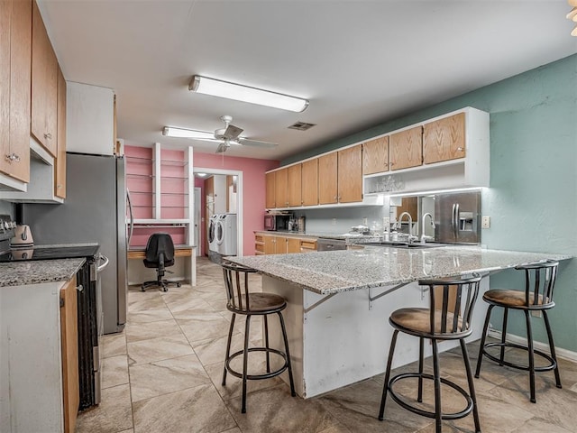 2604 Jeannes Trl, Edmond, OK 73012 - kitchen featuring stainless steel appliances, washing machine and clothes dryer, a peninsula, a kitchen bar, and light stone counters