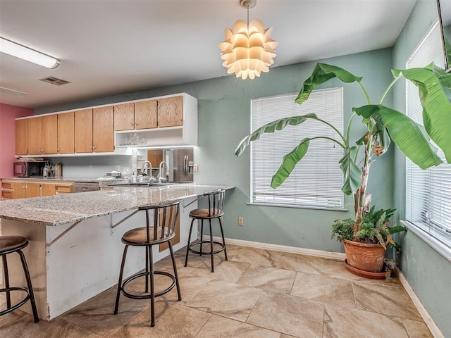 2604 Jeannes Trl, Edmond, OK 73012 - kitchen featuring light brown cabinetry, a breakfast bar, light stone countertops, pendant lighting, and a sink