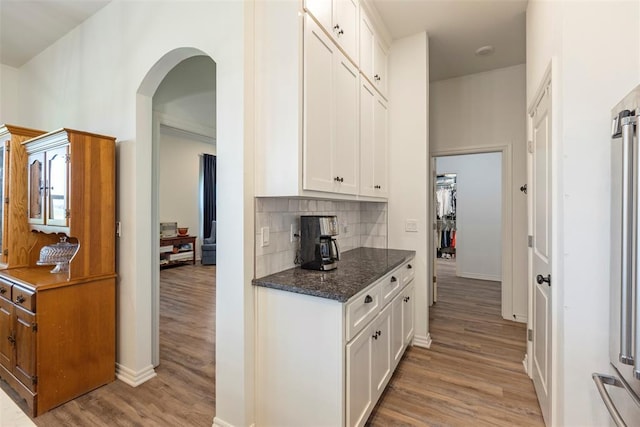 29731 Jade St, Cashion, OK 73016 - kitchen with light wood finished floors, arched walkways, white cabinetry, backsplash, and dark stone countertops