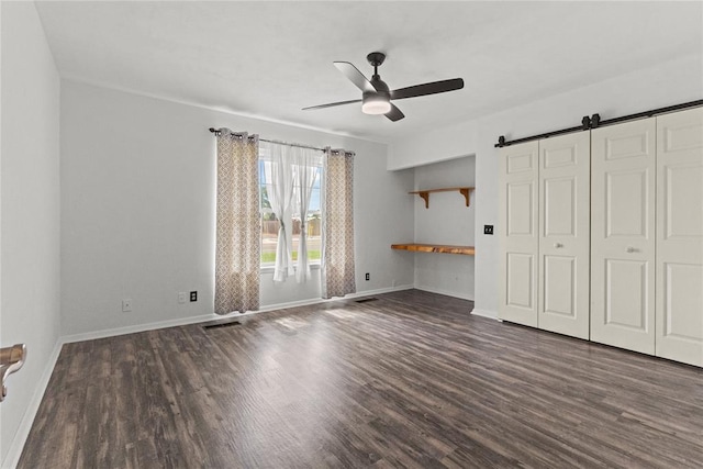 2020 Lyle Rd, Weatherford, OK 73096 - unfurnished bedroom featuring dark wood-style floors, a barn door, baseboards, a ceiling fan, and a closet